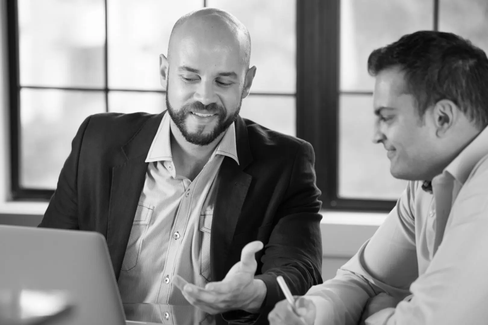 Two men are sitting at a table and one is holding a pen.