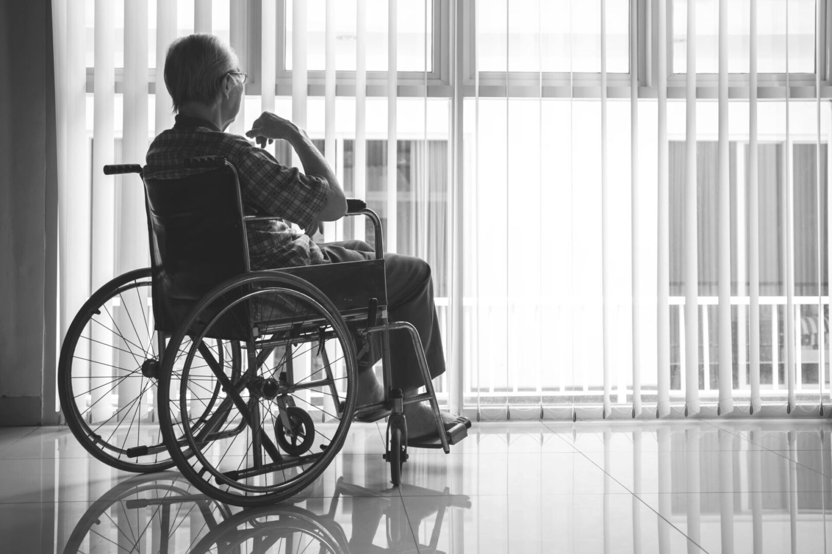 Back view of elderly man looks pensive while sitting in the wheelchair by the window. Shot in the retirement home